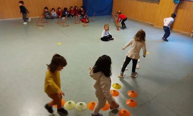 Bambini si divertono con giochi psicomotricità 3 anni: corrono, saltano ostacoli e camminano su coni colorati in palestra.