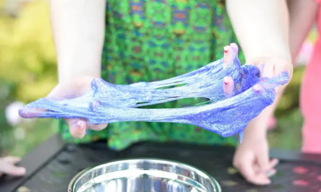 Mani che creano slime glitterato viola, un divertente esperimento su come si fa lo slime.