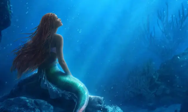 La sirenetta storia breve: una giovane sirena dai capelli rossi guarda verso l'alto, sognando il mondo di sopra, seduta su una roccia sottomarina.