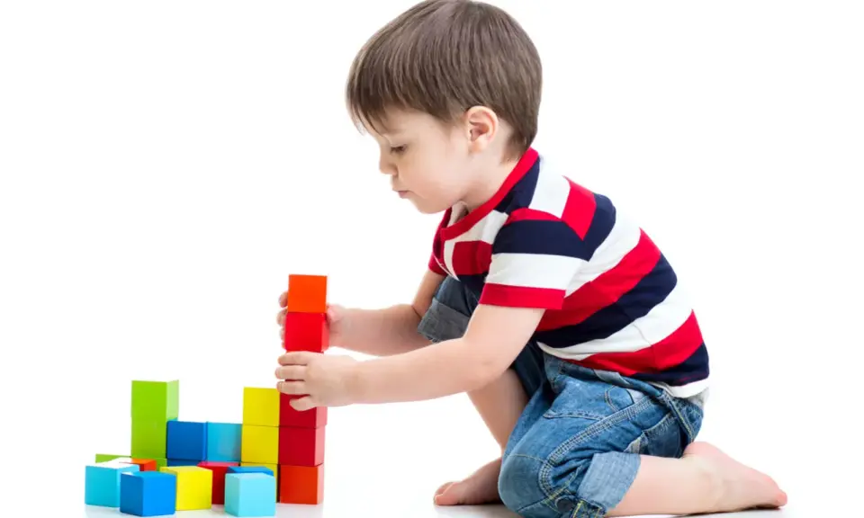 Bambino costruisce torre con blocchi colorati, esercitando la motricità fine. Obiettivi per lo sviluppo cognitivo e manuale.