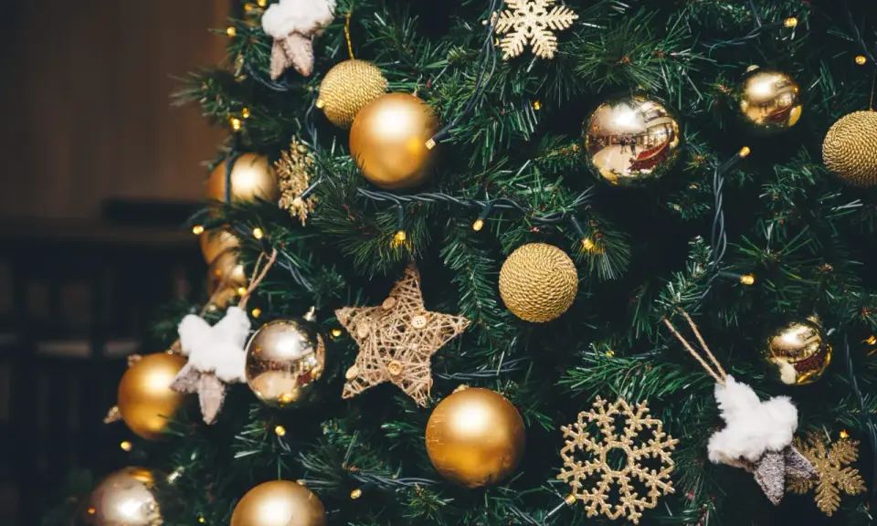 Un albero di Natale addobbato con palline dorate, fiocchi di neve scintillanti e stelle di stoffa. Le luci gialle creano un'atmosfera magica, un vero simbolo albero di natale.