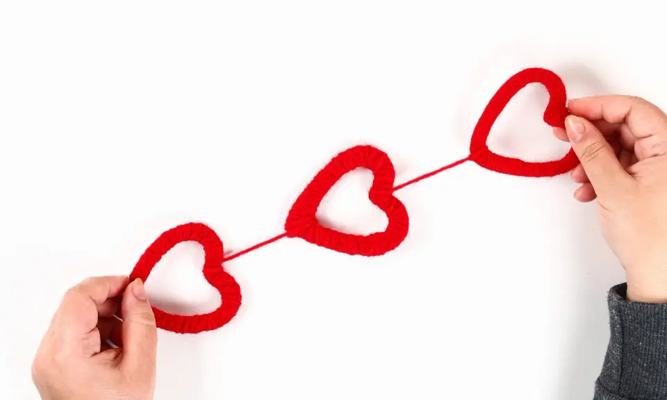 Mani che creano cuori rossi di lana, perfetti per lavoretti per San Valentino.