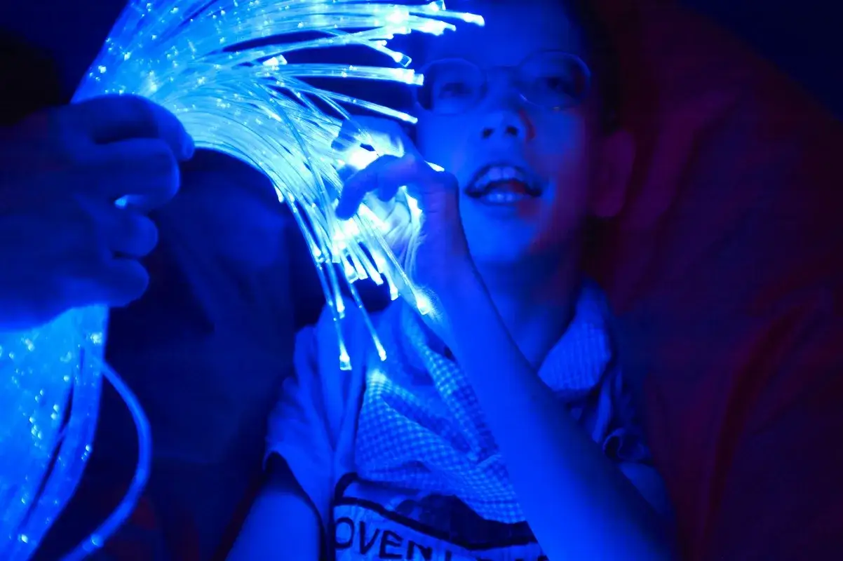 Bambino con occhiali interagisce con fibre ottiche luminose, un'esperienza multisensoriale per disabili gravi.