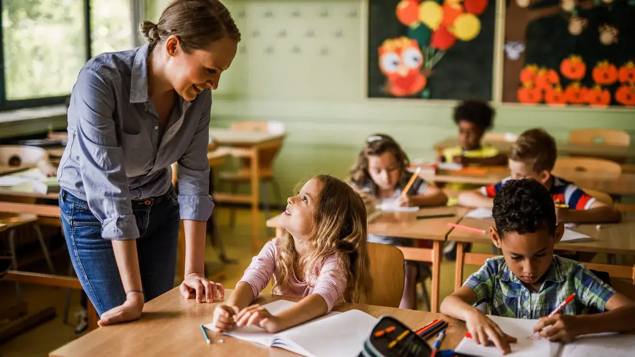 Insegnante sorridente interagisce con una bambina in classe. Un esempio di come il modeling cos'&egrave;: imparare osservando e interagendo.