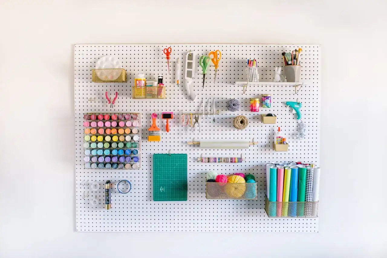 Organizzazione creativa con schemi chiodini gioco: colori, forbici, pennelli e filati pronti all'uso su pannello forato.