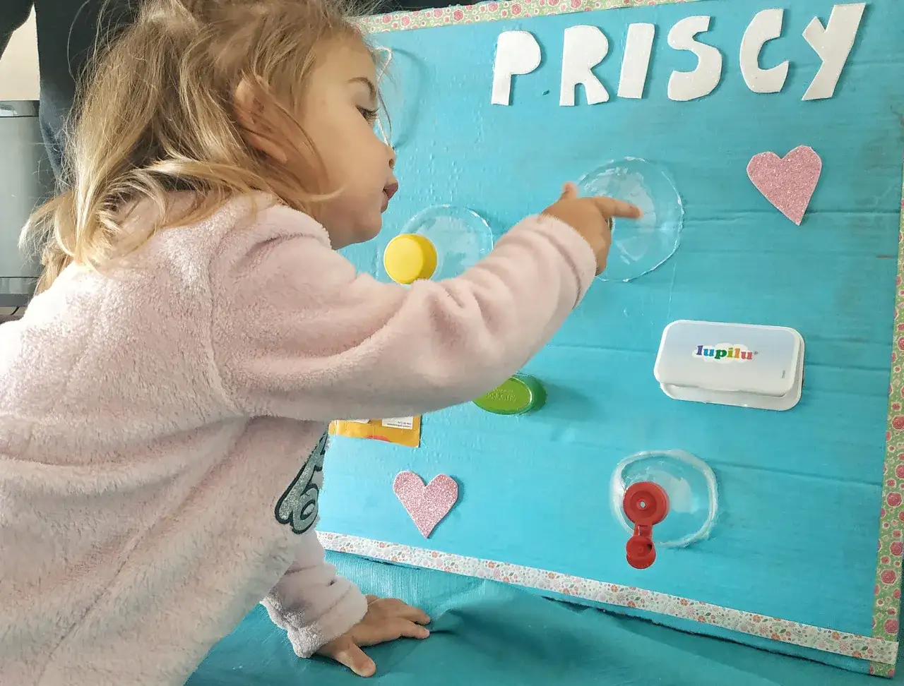 Bambina interagisce con giochi motricità fine fai da te su pannello azzurro con lettere 