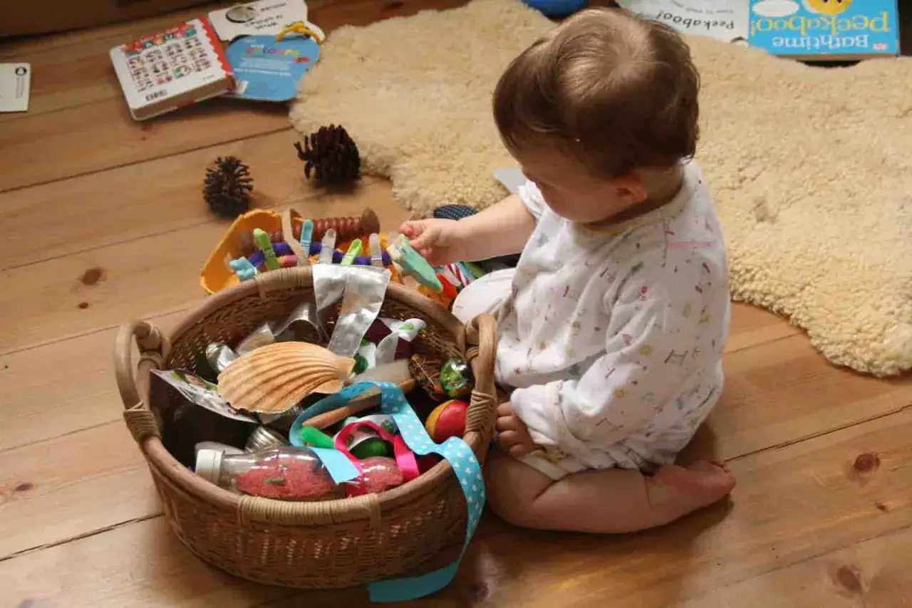 Bambino esplora un cestino dei tesori fai da te pieno di oggetti naturali e riciclati, come conchiglie e pigne.