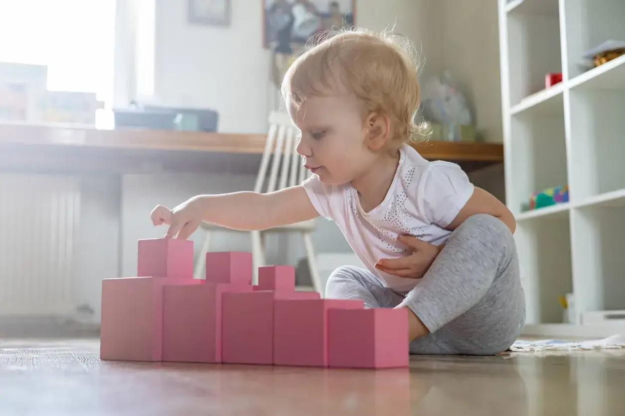 Bambina di 1 anno gioca con blocchi rosa, un'attivit&agrave; divertente in casa per sviluppare la coordinazione.
