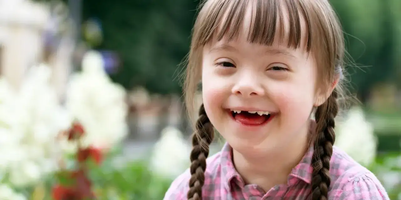 Bambina sorridente con trecce, che mostra la sua gioia. La sindrome di Down lieve si riconosce anche da un sorriso così radioso.