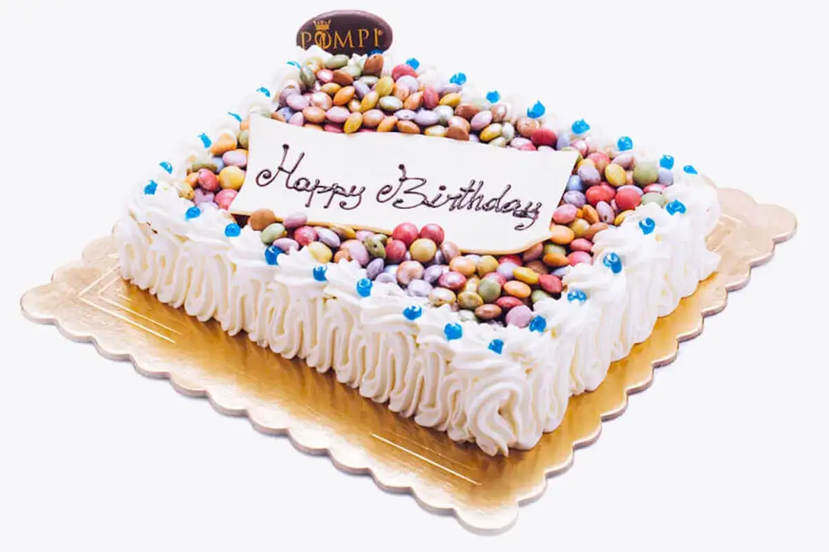 Torta compleanno rettangolare con glassa bianca, decorata con caramelle colorate e la scritta 