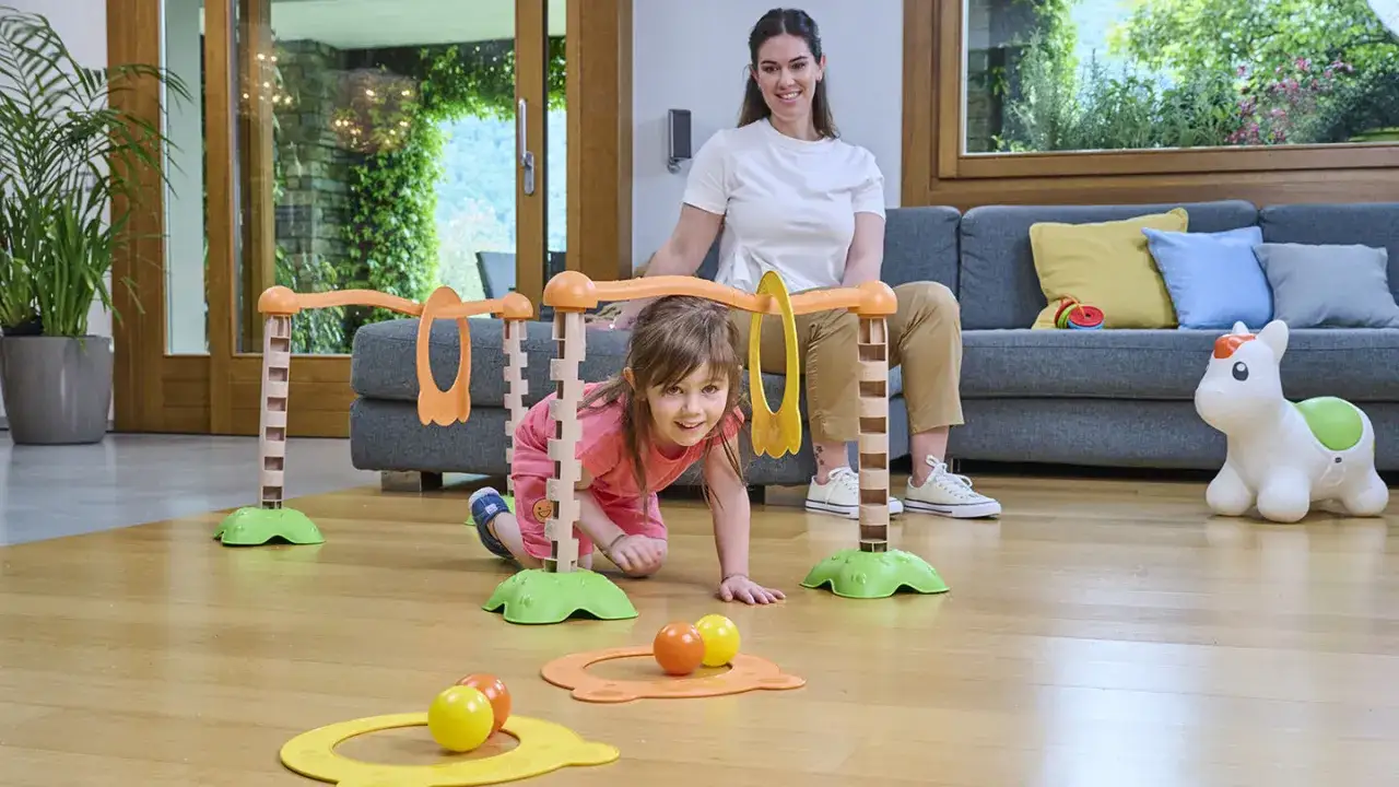 Bambina si diverte gattonando tra giochi psicomotricità 3 anni, con mamma che osserva.