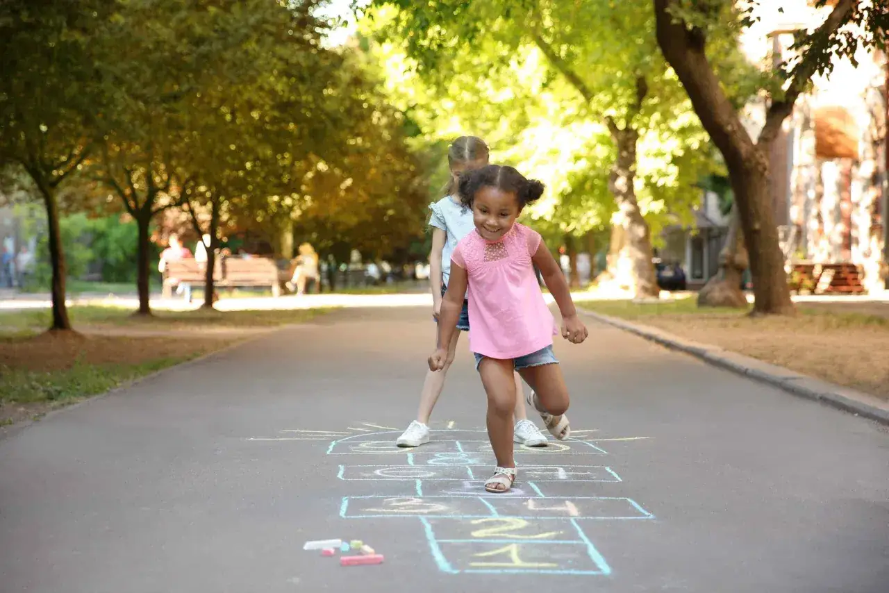 Bambine giocano alla campana, un classico dei giochi di una volta all'aperto, in una giornata di sole.