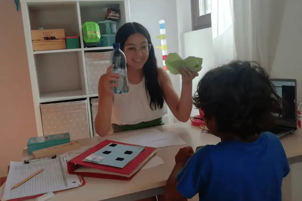 Logopedista con bambino, impegnati in divertenti logopedia esercizi con una bottiglia d'acqua e un oggetto verde.