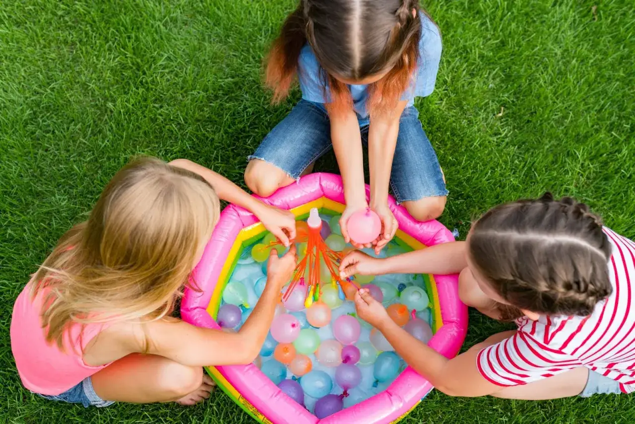 Bambine giocano con palloncini d'acqua in una piscina gonfiabile, perfetti giochi bambini 6 anni compleanno all'aperto.