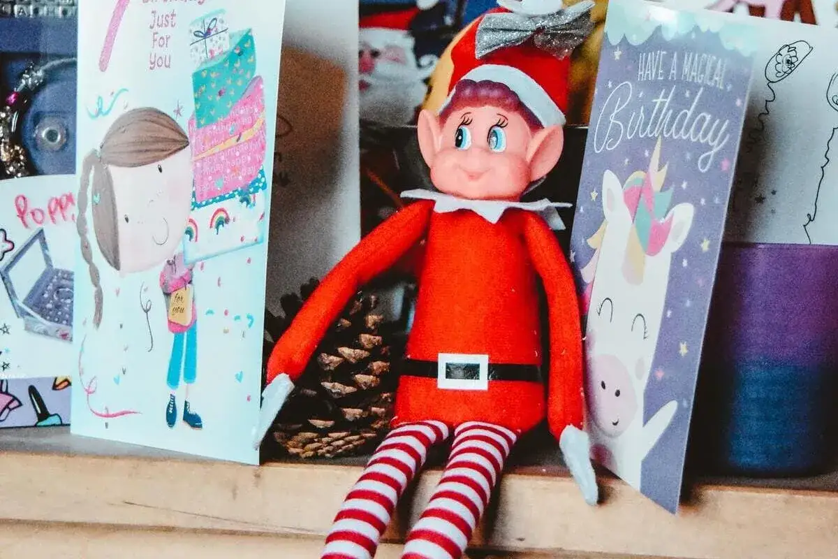 Un elfo di Natale, con il suo vestito rosso e calze a righe, è seduto tra biglietti d'auguri. La sua storia è legata alla magia del Natale e dei compleanni.
