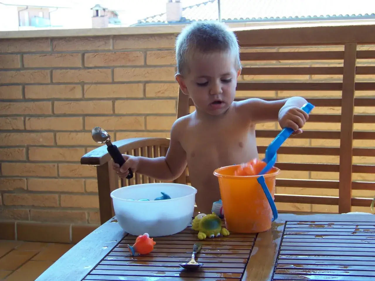 Bambino si diverte con secchiello e palette, creando allegri giochi d'acqua sul tavolo di legno.