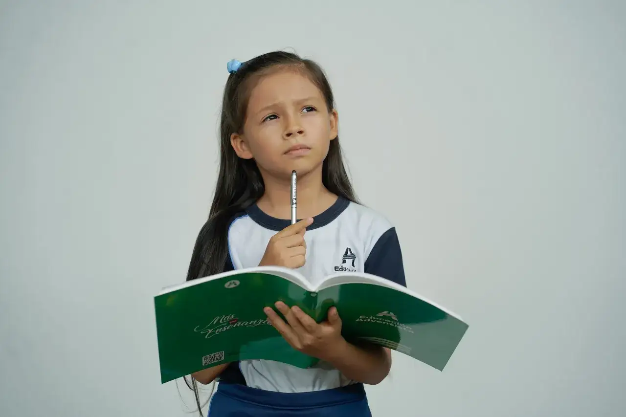 Bambina pensierosa con libro aperto, cerca la risposta a 100 indovinelli.