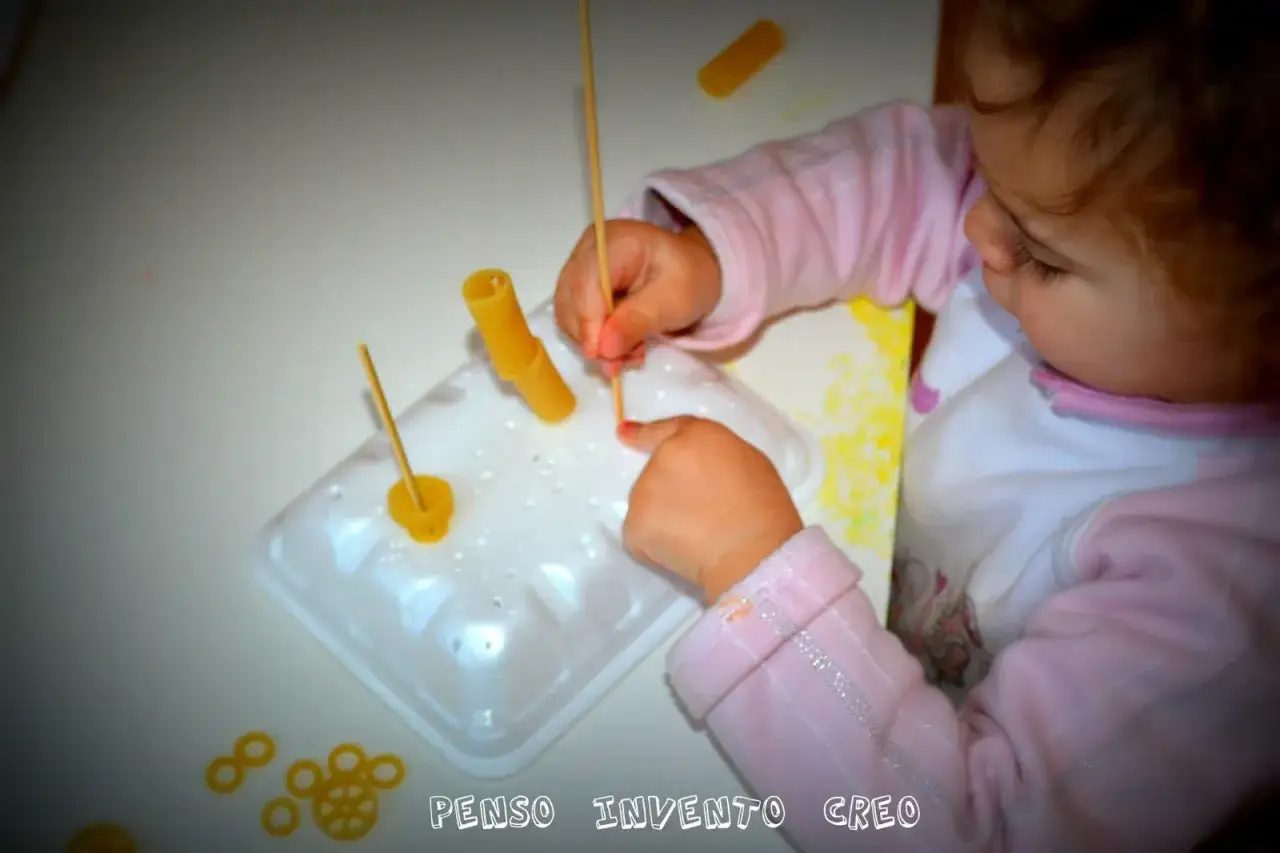 Bambina di 3 anni si diverte con giochi creativi: infila pasta su stuzzicadenti.