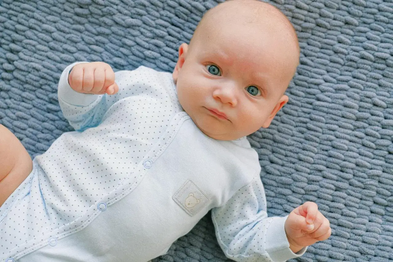 Un neonato con occhi azzurri e un pigiamino a pois. Il suo sguardo intenso è un riflesso di moro autismo, un mondo interiore da scoprire.
