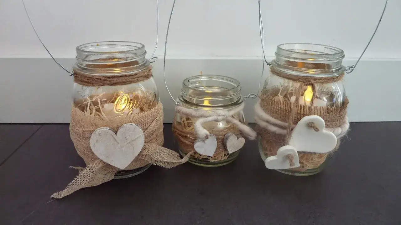 Tre vasetti lanterne fai da te decorati con cuori e spago, con candele accese all'interno per un'atmosfera calda.
