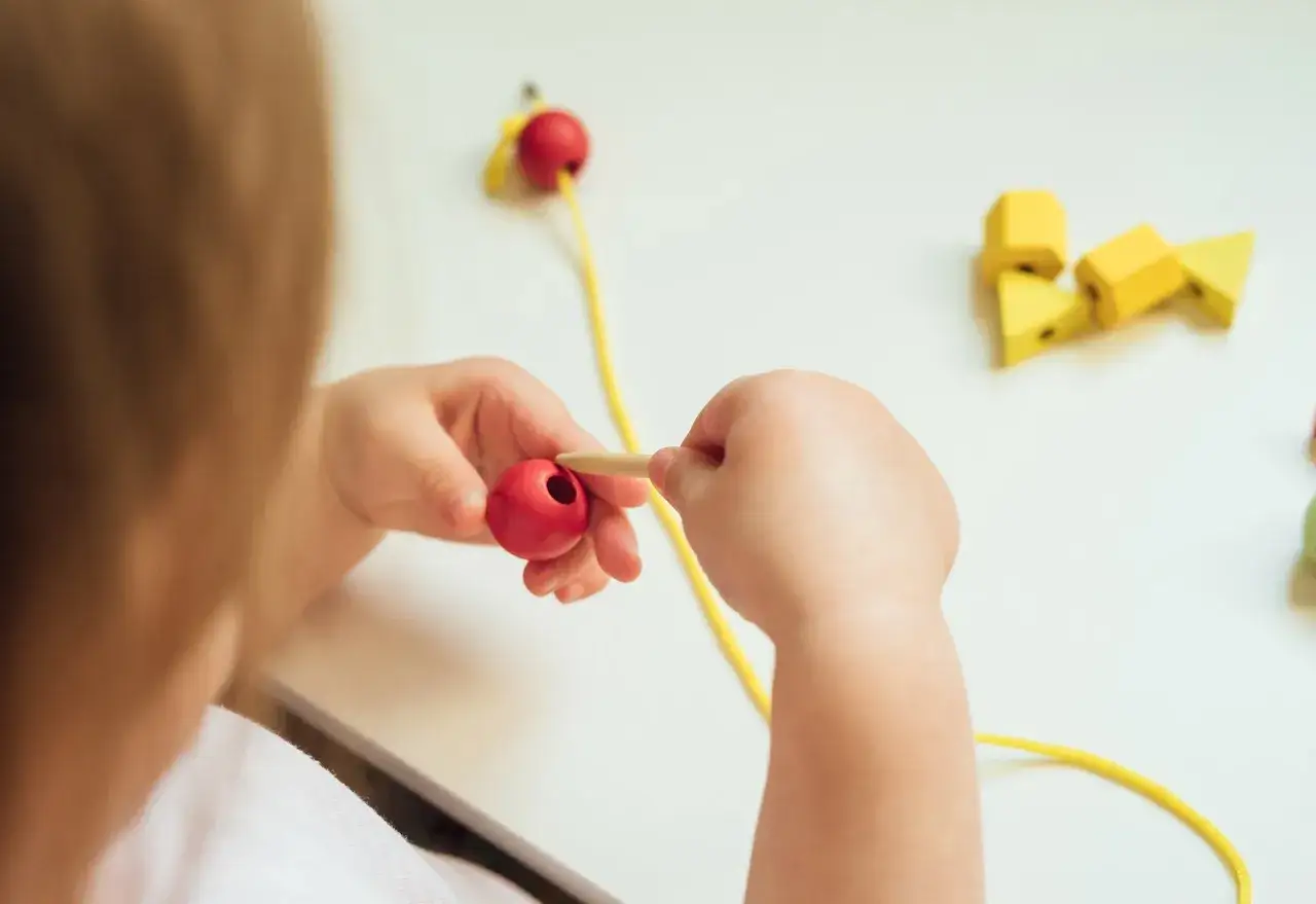 Bambino infila perle rosse, esercitando la motricit&agrave; fine. Obiettivi pei per lo sviluppo.