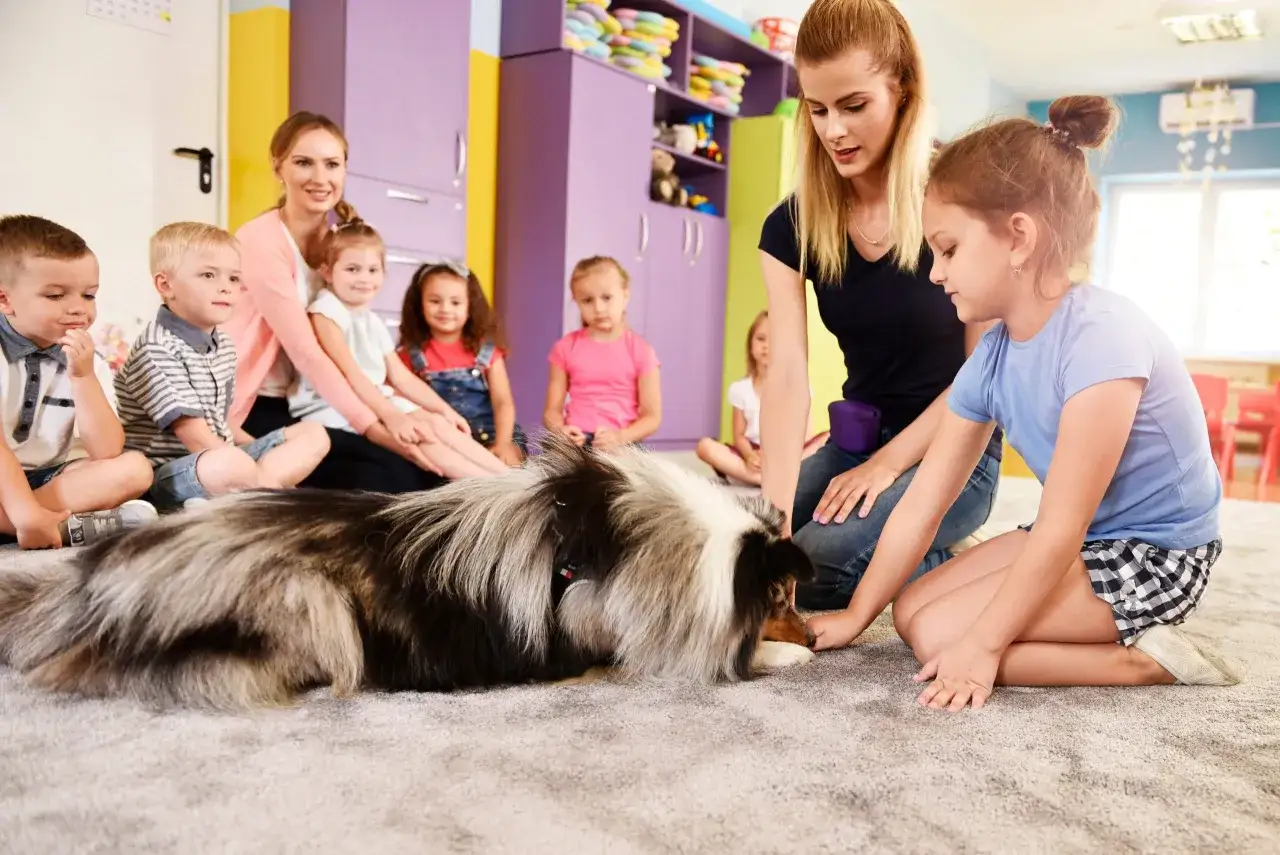 Bambini e un cane peloso partecipano a una sessione di pet therapy in una stanza colorata.