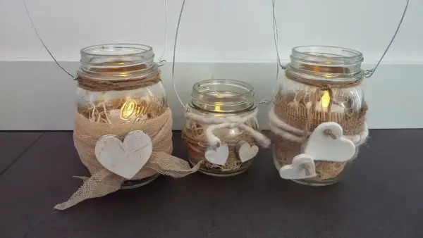 Tre vasetti lanterne fai da te decorati con cuori e spago, con candele accese all'interno per un'atmosfera calda.