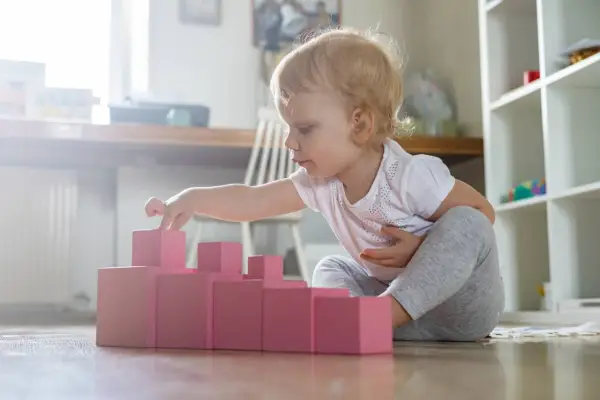 Bambina di 1 anno gioca con blocchi rosa, un'attività divertente in casa per sviluppare la coordinazione.